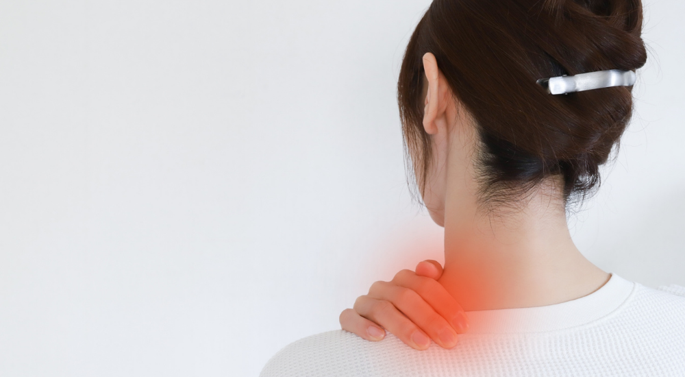 女性の後ろ姿で、【首の付け根から肩（僧帽筋上部付近）】が赤くハイライトされており、強い肩こりや炎症の痛みを抱えている様子。
